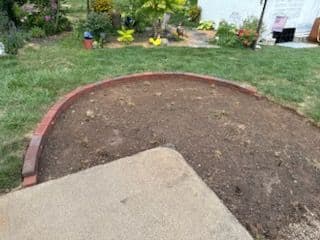 Curved brick border around bare soil in backyard garden ready for planting.