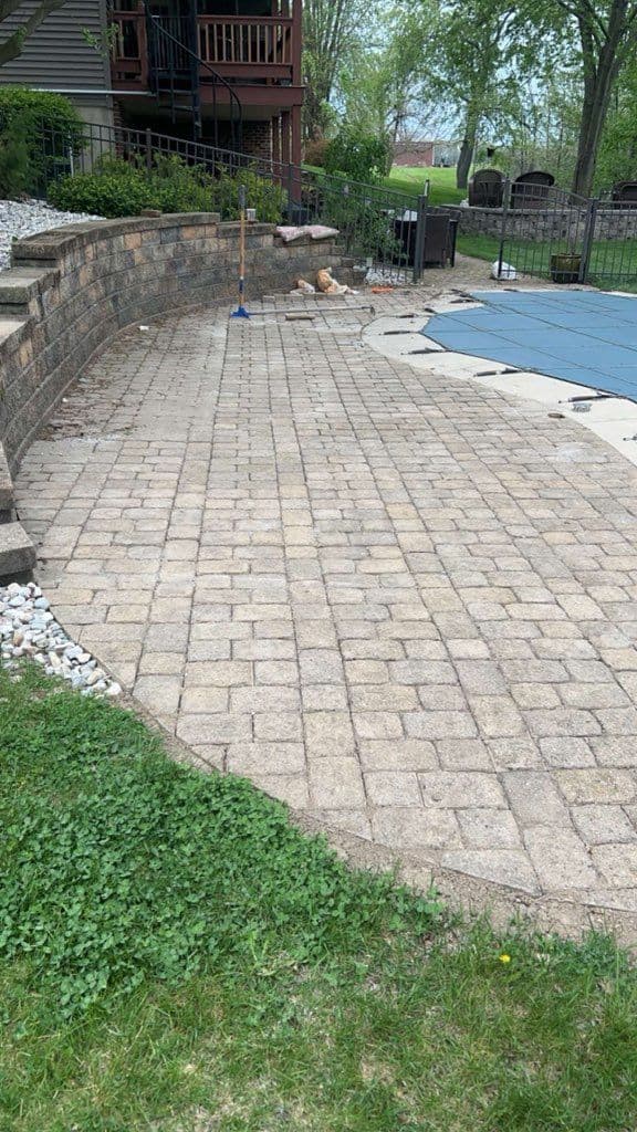 Patio area with brick paving, grass edge, and a pool cover in a residential backyard.