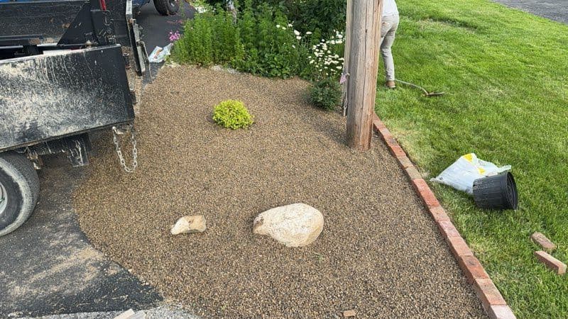 Gravel landscaping with large stones and plants near a driveway and utility pole.