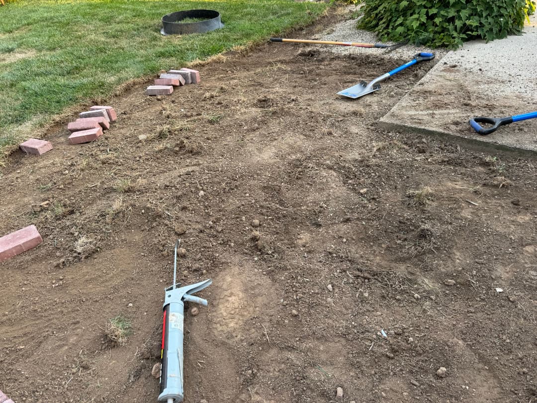 Gardening tools and bricks on a dirt patch ready for landscaping project.